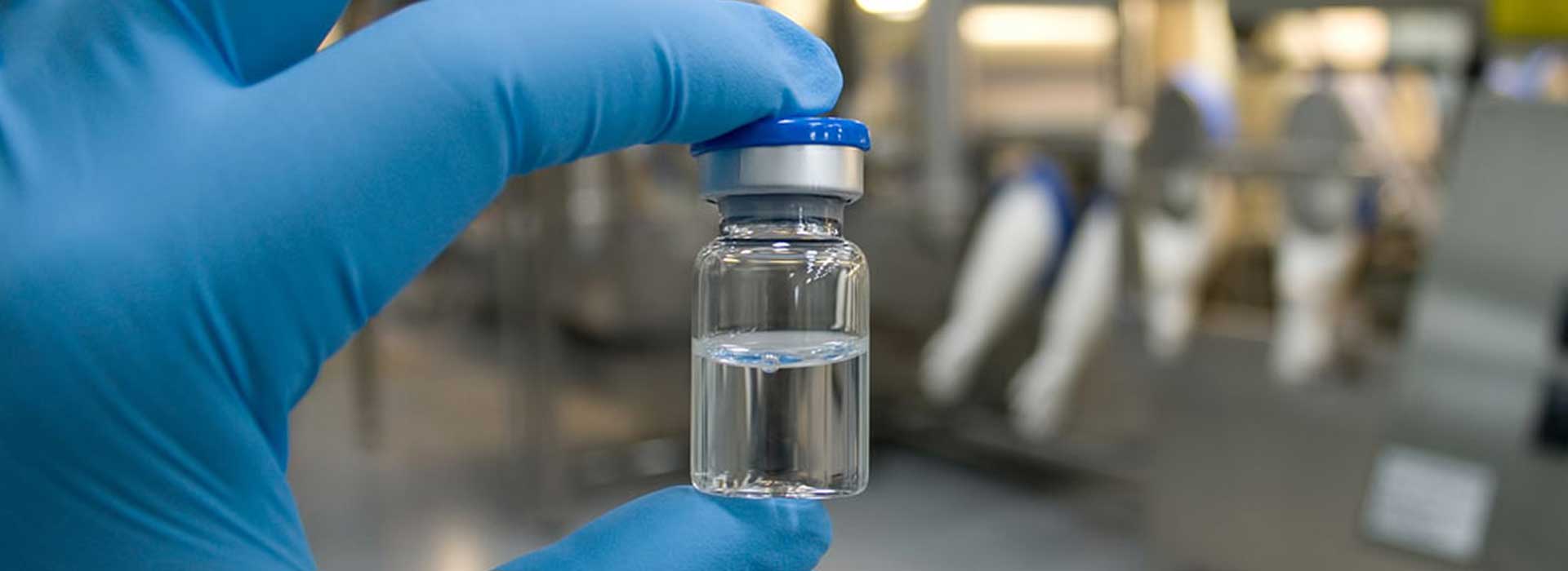 Blue latex glove holding a small vial half filled with a clear liquid.